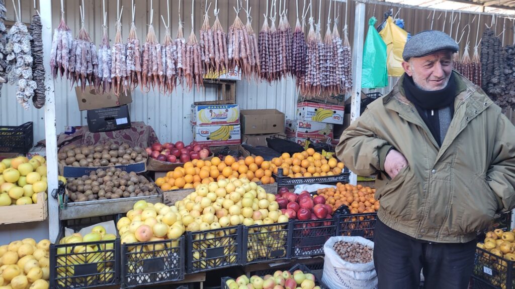 Mężczyzna stoj przy owocać w kurtce i czapce, bazar, Tbilisi, Gruzja