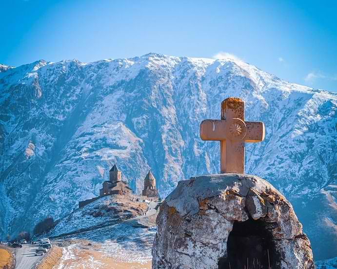 Krzyż rzeźbiony na tle monastyru Gergetis Sameba i zaśnieżonych gór w regionie Kazbegi, Gruzja. Photo: Paata.ge Photography