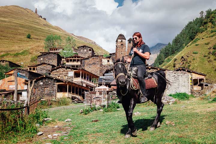 mężczyzna na koniu stoi na tle starej wioski w górach. Tuszetia, Gruzja