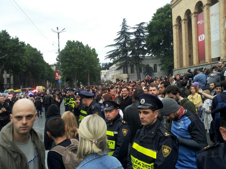 Manifestacja polityczna przed parlamentem na alei Rustawelego w Tbilisi, Gruzja. Dużo ludzi stoi i przechodzi, policjanci tworzą blokadę